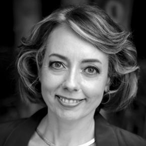A black and white photo of a woman standing outside and smiling.