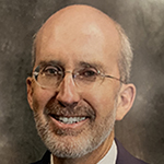 A man with a beard and glasses stands and smiles