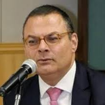 A man wearing glasses and a suit speaks into a microphone.